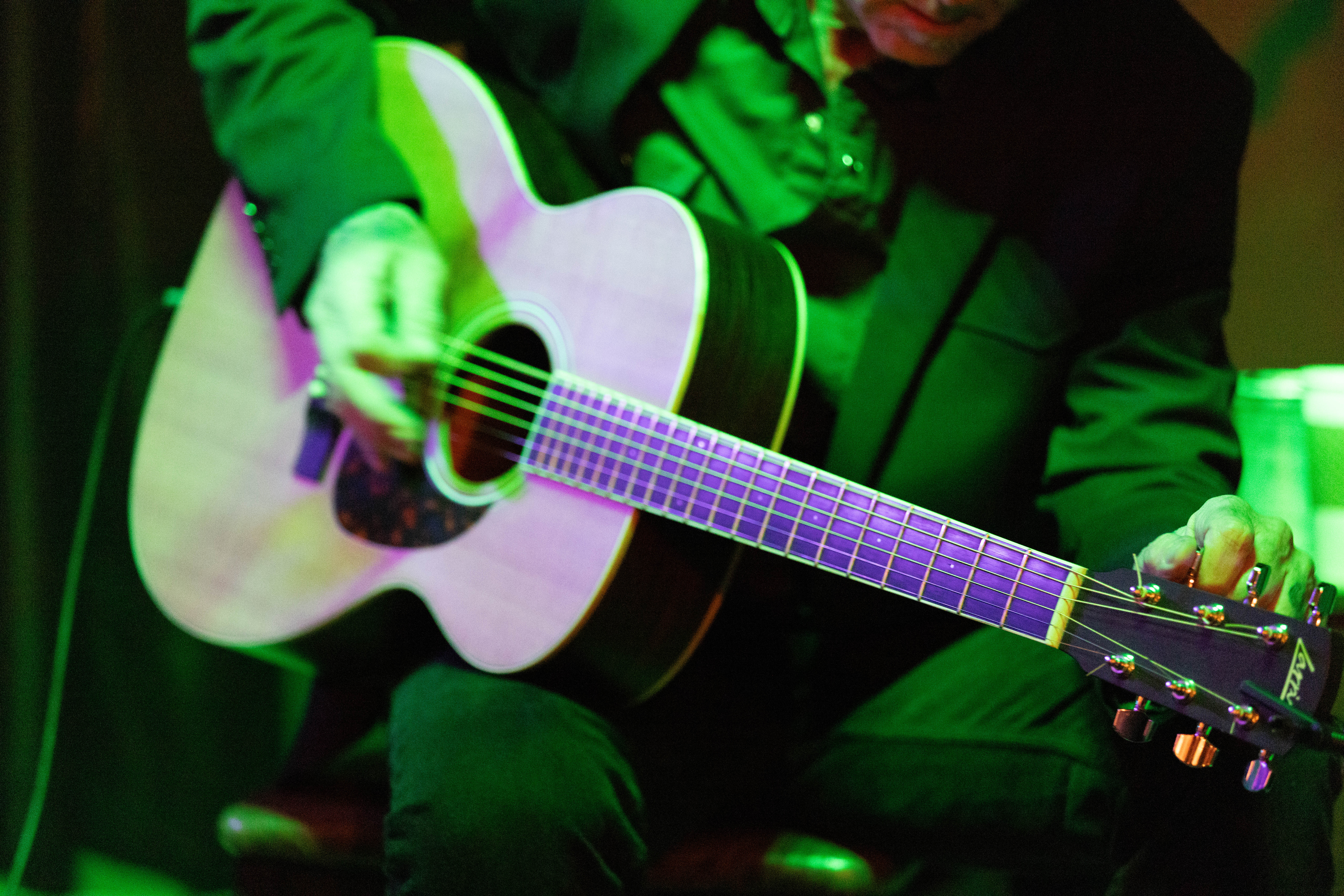 Green-lit guitar hands, intimate close-up of fretwork during performance